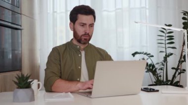 Yetişkin bir erkek, portatif bilgisayarla masanın başında oturmuş düşünceli bir şekilde başka tarafa bakarken e-posta yazıyor. Kafkasyalı serbest yazar üretken çalışma süreci için hafif dairedeki rahat iç ofisi seçti.