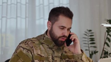 Kafkas askeri üniformalı bir subayın portresi. Akıllı telefonla konuşuyor ve kapalı alanda el kol hareketi yapıyor. Sakallı yetişkin erkek, iletişim için modern mobil aygıt kullanıyor ve askerlere emirler veriyor..