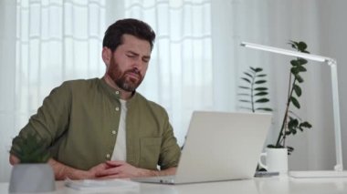Ofisteki laptopta çalışırken aşırı yemek yiyen hayal kırıklığına uğramış erkek serbest yazar portresi. Kafkasyalı üzgün bir adam karnına dokunuyor ve evde rahatsız ve keskin bir ağrı hissediyor..