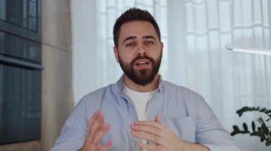 Gündelik kıyafetli beyaz adam portresi kameraya konuşuyor ve arka planda hareketler yapıyor. Çevrimiçi röportaj yapan kendine güvenen erkek çalışanın ev arkadaşı ile bilgisayardan video görüşmesi yapıyor..