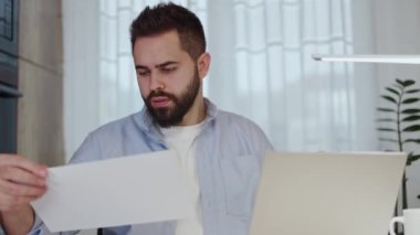Modern dizüstü bilgisayar ve lambayla belgelere bakan konsantre bir adam. Yıllık şirket gider hesaplarının elektronik ve basılı sürümlerini kontrol eden uzaklık finans yöneticisi.