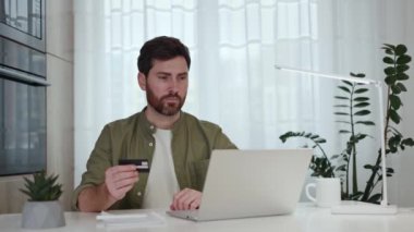 Elinde kredi kartı olan neşeli sakallı adam modern laptopta harika haberler okurken evet hareketi yapıyor. Beyaz tenli serbest çalışan ev ofisinde otururken e-posta üzerinden maaş bildirimi alıyor.