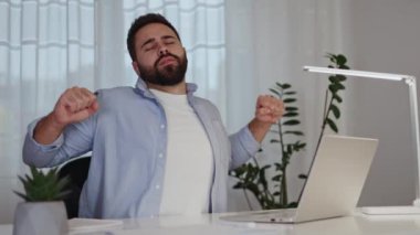 Üretken esmer adam, iş günü boyunca dizüstü bilgisayarla ısınmak ve esnemek için mola veriyor. Uzaktan kumandalı deneyimli programcı evde oturmaktan yorulurken kaslarını rahatlatıyor..