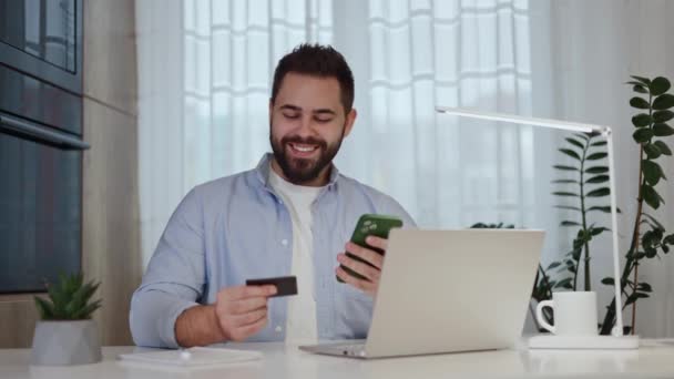 男性兴奋地使用信用卡和手机 而坐在国内台式机与计算机 发大财的人在网上获得贷款许可 并获得账户存款通知 — 图库视频影像