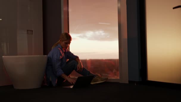 Kadın Yerde Oturup Büyük Pencerenin Arkasında Inanılmaz Günbatımını Izlerken Internetten — Stok video