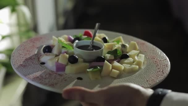 不知名的人手里拿着山羊乳酪盘 配上黑橄榄 沙拉叶和蜂蜜 豪华餐厅大堂服务员向有需求的顾客提供精美的开胃酒 — 图库视频影像
