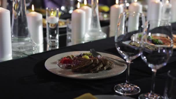 盘子里的美味佳肴在木桌上醒目地陈列在各种配料的前景中 多个白色蜡烛和两个酒杯放在盘子旁边 增添奢华的气氛 — 图库视频影像