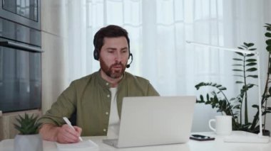 Kafkasyalı serbest çalışan, bilgisayarında video görüşmesi yapan ve ofisteki not defterine bilgi yazan biri. Kablosuz kulaklıklı kendine güvenen adam uzak çalışma süresince yeni iş projesini dinliyor..