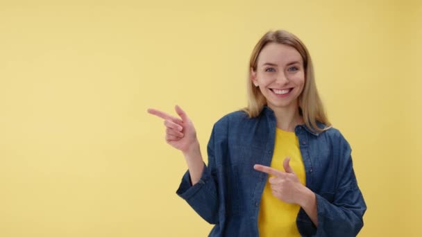 一个快乐的女人的画像 手指指向孤立的黄色墙壁 有复制的空间 快乐的金发女人穿着鲜艳的衬衫和牛仔夹克在工作室做广告 — 图库视频影像