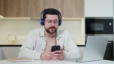 Mutfakta otururken cep telefonu ve taşınabilir bilgisayar kullanan mavi kulaklı, üretken bir erkek. Popüler karışık çalma listesini dinlerken çoklu görev pratiği yapan kaygısız uzak işçi.