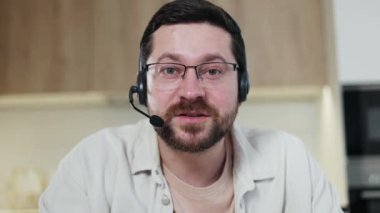 Laptop web kamera görüntüsü, konuşkan erkek, kablosuz kulaklık takıyor ve gözlüklü, modern cihazlar aracılığıyla online video görüşmesi yapıyor. Kafkasyalı bir adam iş arkadaşlarıyla iç işlerinde toplantı yapıyor..