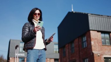 Güneş gözlüklü esmer kadın dışarıda duruyor ve elinde pasaport tutarken cep telefonu kullanıyor. Uluslararası havaalanına taksi beklerken mesajlara cevap veren Kafkasyalı kadın.