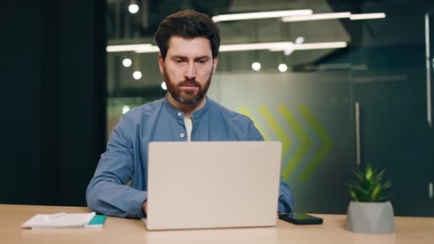 在笔记本电脑上打字时 穿着蓝色衬衫的成年人正对着镜头严肃地看着脸 采用电子设备对财政收入进行有效分析的有重点的男性董事 — 图库视频影像