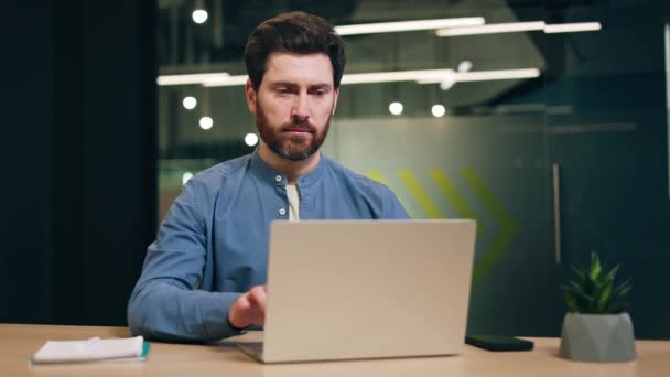 在现代办公室 专业的男性开发人员坐在办公桌前 在笔记本电脑上打字 工作结束后 微笑着看着镜头 叉着胳膊 同时对工作成果感到满意 — 图库视频影像