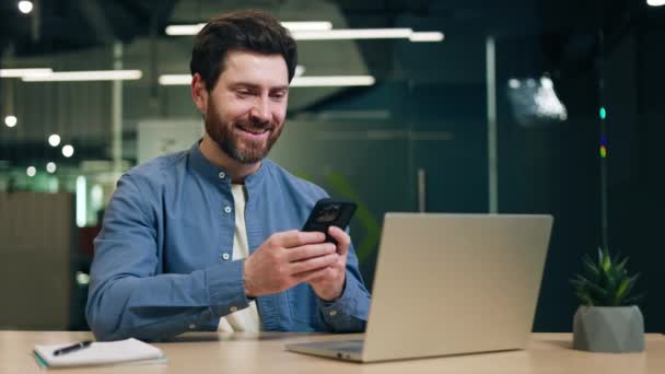 Homem Encantado Segurando Smartphone Olhando Para Tela Enquanto Sentado Mesa — Vídeo de Stock