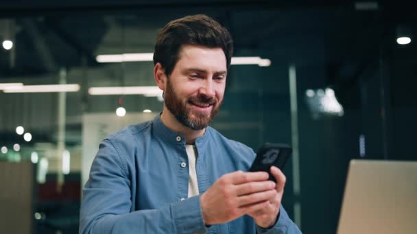 Ofis Masasında Oturmuş Gülümseyen Bir Erkek Çalışan Akıllı Telefondan Oyun — Stok video