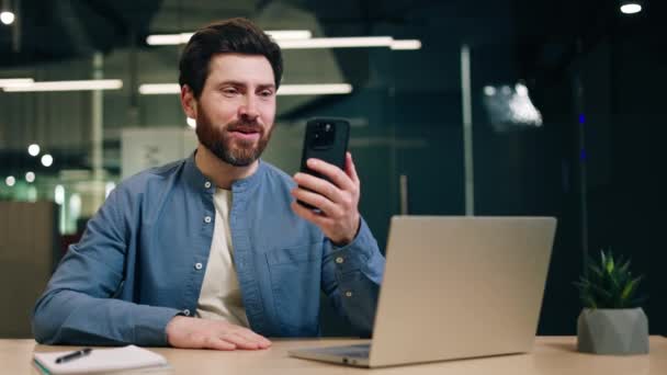 Lächelnder Mann Sitzt Mit Laptop Schreibtisch Und Macht Eine Grußgeste — Stockvideo
