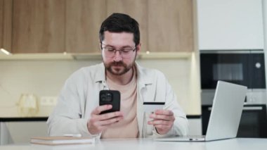 Çevrimiçi akıllı telefondan satın alan yakışıklı bir adam. Beyaz bir erkek kredi kartı tutuyor ve içeride internet alışverişine para harcıyor. Bankacılık ve insanlar kavramı.