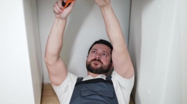 Güçlü odaklı tamirci tişörtün altında yerde yatıyor ve tek gözüyle gözlerini kısarak ingiliz anahtarıyla vanayı sıkıyor. Özenli erkek tesisat tesisatlarını kontrol ediyor..