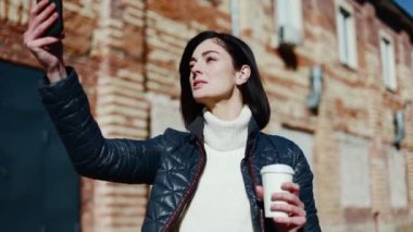 Beyaz balıkçı yakalı endişeli kadın beyaz kahve fincanıyla fotoğraf çekerken dik açı arıyor. Çekici kadın ön kamera için poz veriyor ve yeni profil fotoğrafı için en iyi yıldırımı yakalıyor..