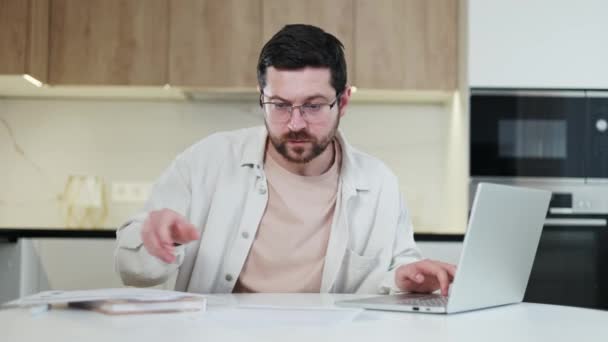 熟練した男性は 重要な文書をレビューし 自宅での作業プロセス中に個人的なノートパソコンを見ています 屋内での距離作業に従事する忙しい白人男性 締め切りと人々の概念 — ストック動画