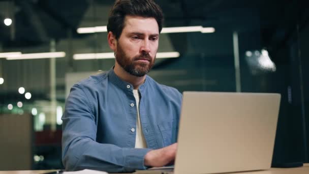 专注的软件开发人员在笔记本电脑上工作 在现代化的协同工作间中 面部表情严肃 多愁善感的男性一边在键盘上打字 一边思考 一边回头看 — 图库视频影像