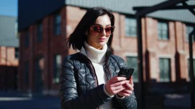 Modern akıllı telefon kullanan sıradan bir kadın ve arka planda dişlek bir gülümsemeyle kameraya bakıyor. Tatmin olmuş kadın ücretsiz halka açık internet bağlantısına başarıyla bağlanıyor.