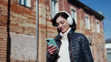 İlkbaharda gezinti sırasında turkuaz çantalı akıllı telefon kullanan, telsiz kulaklıklı tatmin olmuş bir bayan. Sakin bir kadın dinlenirken dinlenme şarkıları eşliğinde şarkı listesini kaydırıyor..
