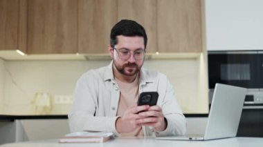 Kafkas erkek uzaktan kumandalı çılgın işçi mutfak ortamında kişisel akıllı telefonuna bakarken birinci sınıf jest yapıyor. Duygusal erkek, teneffüste internetten piyango kazanıyor..
