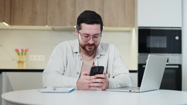 Homem Caucasiano Pensativo Óculos Navegando Smartphone Moderno Enquanto Sentado Mesa — Vídeo de Stock
