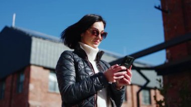 Güneş gözlüklü neşeli bayan cep telefonu ekranına bakıyor ve kahkahalarla zıplarken kazanan el hareketi yapıyor. Çevrimiçi mobil oyunun zor seviyesini tamamlarken güzel bir kadın kendinden geçiyor..