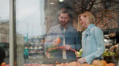 Süpermarketten elma seçen sevimli çiftin panoramik penceresinden izleyeceğiz. Sevimli beyaz insanlar sevimli sohbetler yapıyorlar ve taze meyveleri kapalı mekandan seçiyorlar. İlişki kavramı.