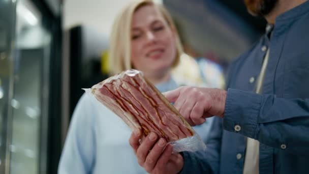 友好的高加索夫妇检查肉类包装 并评估其质量或检查价格在杂货店 冰箱架子的背景在室内 采购和超级市场的概念 — 图库视频影像