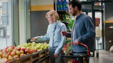 Çekici bir kadın sebze bölümünden elma seçiyor ve sakallı koca tarafından tutulan alışveriş sepetine koyuyor. Süpermarkette romantik bir atmosfer ve birlikte zaman..