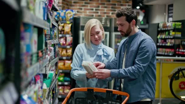 スーパーマーケット内のショッピングカートの隣に立っている間 2人の人が店で買い物をします 棚にさまざまな商品が展示されています 時間のコンセプト — ストック動画