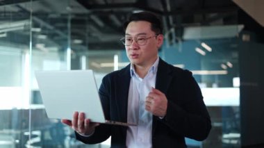 Zarif kostümlü ve gözlüklü bir adam taşınabilir laptop tutarken video konferansında konuşma yapıyor. Japon iş danışmanı ortaklarla çevrimiçi görüşme yapıyor ve sözleşmenin detaylarını tartışıyor.