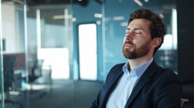 Ofisteki modern koltuğa yaslanan yorgun beyaz iş adamı. Yorgun yüz ifadesi olan sakin bir erkek evde zorlu bir iş gününden sonra dinlenmeye ve dinlenmeye zaman ayırıyor..