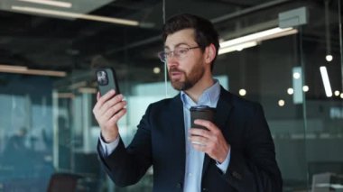 Becerikli erkek yönetici, kişisel ofis içindeki modern akıllı telefondan online video görüşmesi yapıyor. Sakallı beyaz iş adamı dijital cihazdaki konuşma sırasında zihni açıklıyor.