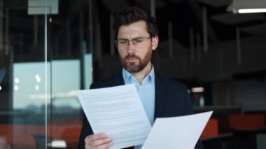 Ciddi bir şirket yöneticisi elinde belgelerle içeride çalışan kişilerin ifadelerini okuyor. Şahsi kabinede dururken kağıt işleriyle uğraşan neşeli beyaz iş adamı. İşgal kavramı.