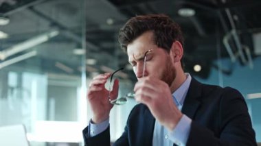 Modern ofiste üzgün erkek portresi, gözlük ve masaj tapınakları çıkarıyor. Evde taşınabilir dizüstü bilgisayar üzerinde çalışırken baş ağrısı çeken umutsuz beyaz bir adam. İş dünyası.