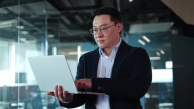 Moda ceketli bir adam taşınabilir dizüstü bilgisayar tutuyor ve klavyeye mesaj yazıyor. Ofis odasındaki online projeyi bitirdikten sonra kameraya bakıp gülümseyen başarılı bir yönetici..