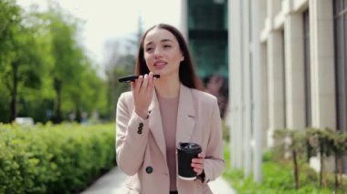 Çekici bir kadın, halka açık alanda yürürken arkadaşlarıyla iletişim kurmak için modern cihazlar ve internet kullanıyor. Tarz sahibi bir kadın telefonla konuşurken bir fincan kahveden zevk alıyor..