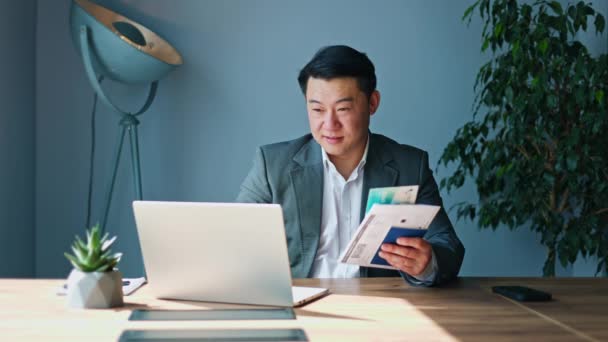 Trabalhador Chinês Sorridente Digitando Laptop Portátil Olhando Para Bilhetes Impressos — Vídeo de Stock