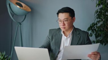 Ciddi bir iş adamı, kişisel çalışma yerindeki belgeleri incelerken taşınabilir dizüstü bilgisayarda özenle yazıyor. Rafine edilmiş resmi giysiler içinde sakin erkek giysileri işgalin derinlerine işlemiş..