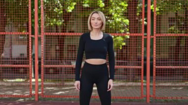 Siyah etek giyen fit bir kadın antrenmandan önce boynunu esnetir ve fiziksel aktiviteye hazırlanır..