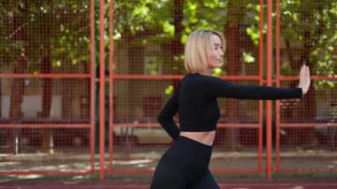 Siyah spor kıyafetli fit bir kadın esneyip dışarıda ısınma egzersizi yapıyor..