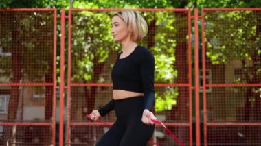 Siyah spor giyim giymiş bir kadın şehir parkında ip atlıyor. Fitness, spor ve sağlıklı yaşam tarzı konsepti