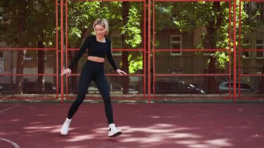 Genç bir kadın dışarıda basketbol sahasında spor yapmaya hazırlanıyor..