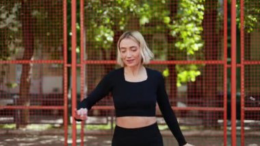 Siyah spor giysili genç bir kadın antrenmandan önce ısınıyor. Gülümsüyor ve yana bakıyor..