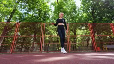 Genç bir kadın açık hava fitness seansı için ısınıyor. Siyah spor ayakkabı ve beyaz spor ayakkabı giyiyor..